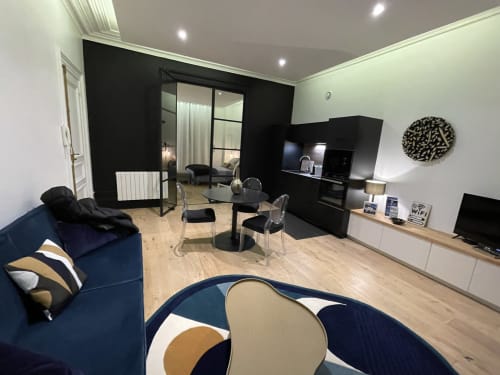 Séjour moderne aux Gîtes Boulogne Sur Mer : canapé bleu marine, table à manger, kitchenette et chambre en arrière-plan
