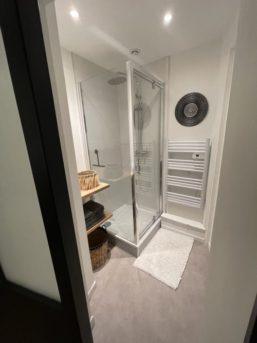 Salle de bain moderne avec douche vitrée, porte-serviettes chauffant et miroir circulaire décoratif aux Gîtes Boulogne Sur Mer