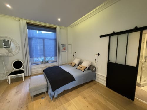 Chambre moderne aux Gîtes Boulogne Sur Mer avec lit, porte grange coulissante, fenêtre avec vue sur un monument, et parquets en bois