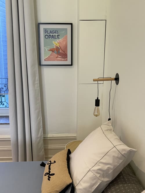 Chambre cosy aux Gîtes Boulogne-sur-Mer : oreiller blanc, lampe suspension en bois et affiche vintage de plage sur mur crème