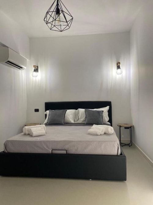 Camera moderna a La Maison Srls a Bari con letto platform nero, plafoniera geometrica e pareti bianche minimaliste