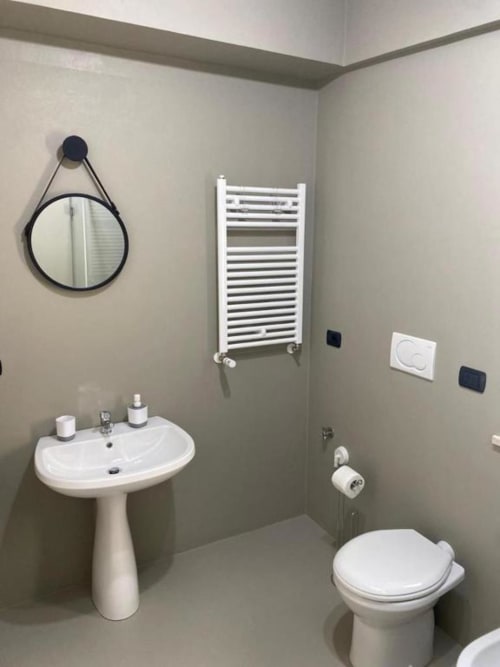 Bagno moderno nell'appartamento La Maison Srls a Bari con lavabo a colonna, wc bianco, scaldasalviette e specchio rotondo