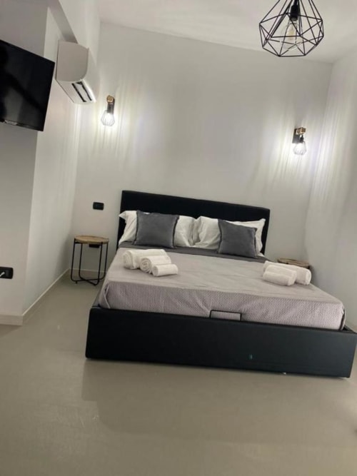 Camera da letto moderna a La Maison a Bari con letto nero, pareti bianche, lampada a sospensione geometrica e arredi contemporanei