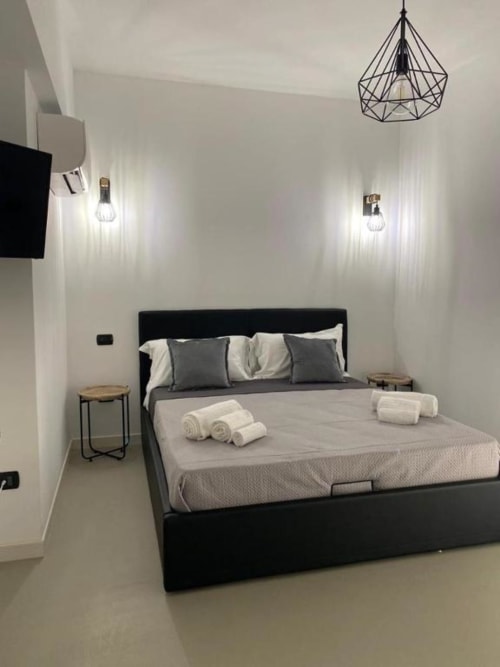 Camera moderna di La Maison Srls a Bari con letto nero, pareti bianche, lampada geometrica e asciugamani arrotolati