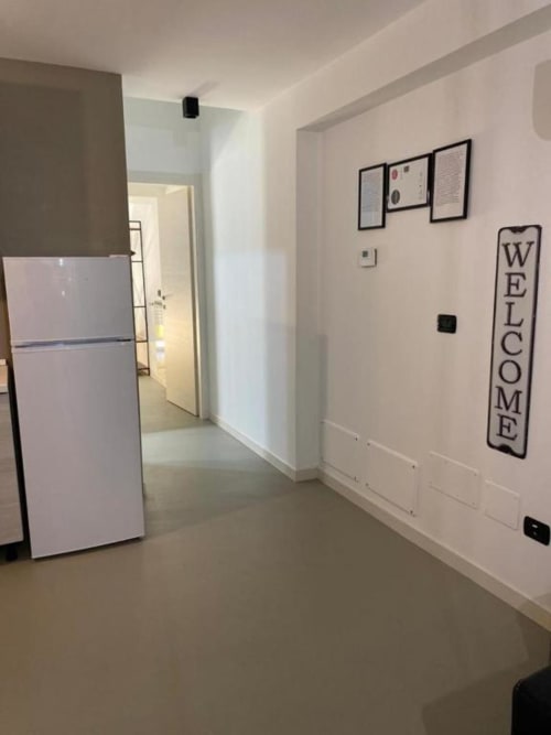 Corridoio moderno di La Maison Srls a Bari con pareti bianche, frigorifero, cartello di benvenuto e documenti incorniciati.
