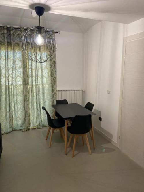 Moderna zona pranzo di La Maison a Bari con tavolo nero, sedie in legno, lampadario sospeso e tende a motivi verdi