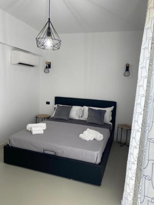 Camera da letto moderna a La Maison di Bari con letto nero, biancheria grigia, lampada geometrica e arredamento minimalista