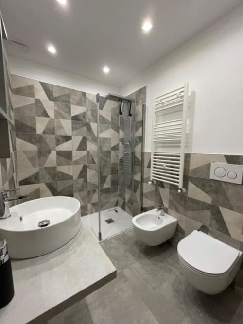 Bagno moderno con doccia in piastrelle geometriche, sanitari bianchi, scaldasalviette e illuminazione incassata a Villa La Maison, Bari