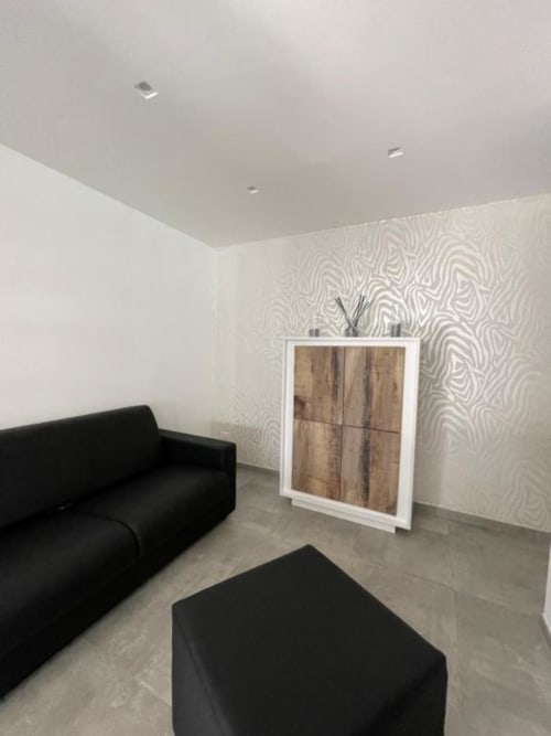 Elegante salotto di villa moderna presso La Maison con divano nero, carta da parati decorativa e mobile in legno a Bari