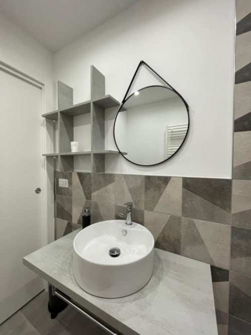 Elegante mobile da bagno con specchio rotondo e piastrelle geometriche nella villa La Maison a Bari