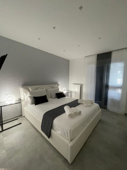 Camera moderna di Villa La Maison a Bari con letto bianco, dettagli neri e finestre con vista sul giardino