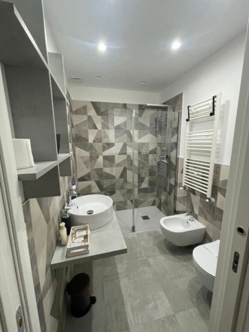 Bagno moderno a La Maison villa a Bari con doppio lavabo, doccia walk-in, scaldasalviette e dettagli geometrici in ceramica