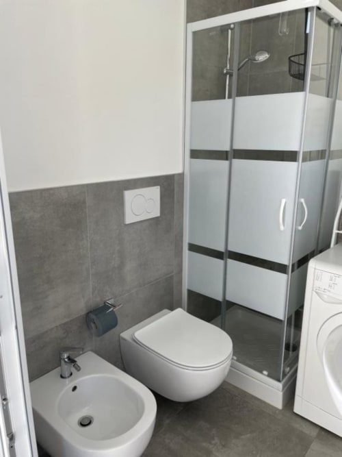 Bagno moderno di La Maison villa a Bari con piastrelle grigie, bidet e water bianchi, doccia con box in vetro