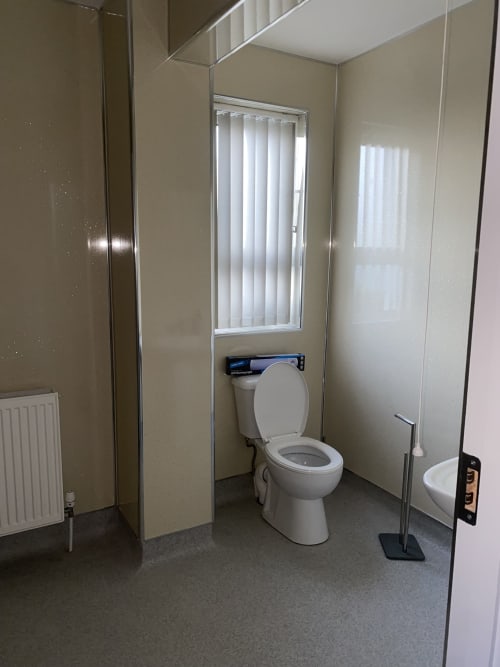 Modern bathroom at Duffy Lodge apartment in Co. Donegal with white toilet, sink, shower enclosure and vertical blinds window.