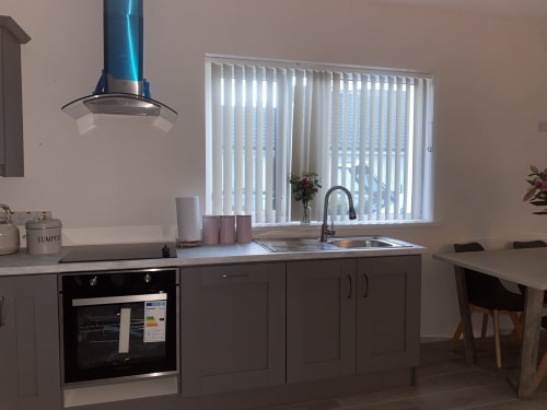 Modern kitchen in Duffy Lodge apartment, Co Donegal with stainless steel sink, oven, dark cabinets and vertical blinds over