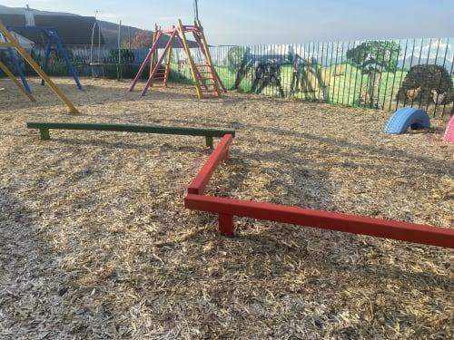 Outdoor playground at Duffy Lodge in Co Donegal with red seesaw, climbing wall, and wooden play equipment on bark mulch