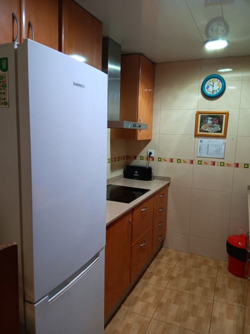 Modern kitchen with white Daewoo refrigerator, wooden cabinets, and tile walls in Casa Ferrer Barcelona apartment