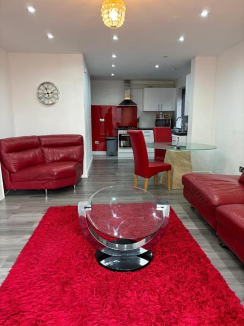 Modern open-plan living area with red leather furniture, glass coffee table, and kitchen with red cabinetry at Sunbeam Haven