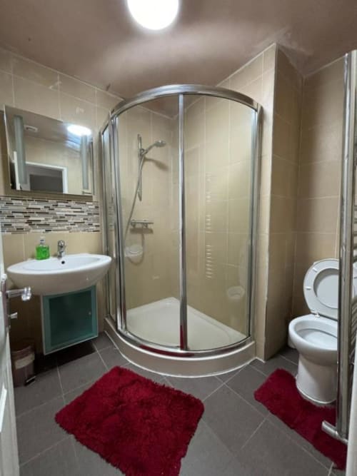 Modern bathroom in Sunbeam Haven bungalow with curved shower enclosure, white sink, toilet, red bath mats, and cream tiled