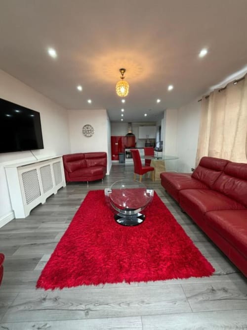 Modern living room at Sunbeam Haven bungalow in High Wycombe with red leather sofas, flat-screen TV, and red rug.
