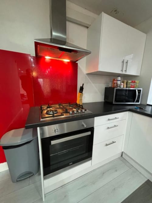Modern kitchen with white cabinets, black countertop, red backsplash, gas hob, and stainless steel hood in Sunbeam Haven