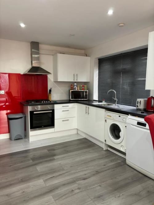 Modern kitchen in Sunbeam Haven bungalow with white cabinets, red backsplash, black countertops, washing machine, and wood
