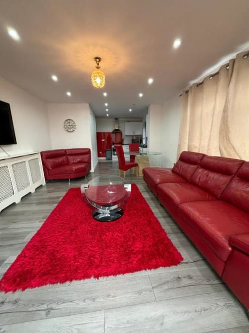 Modern living room at Sunbeam Haven villa in High Wycombe with red leather sofas, rug, and open-plan kitchen