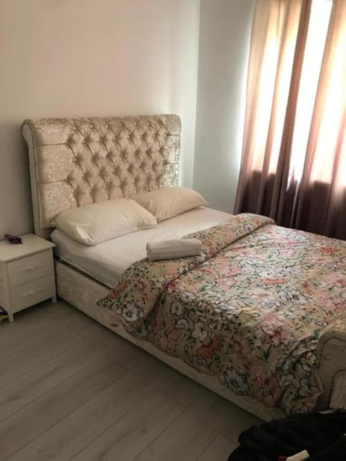 Bedroom at Sunbeam Haven 2BR Bungalow with beige upholstered bed, floral bedding, pillows, bedside table, and garden view