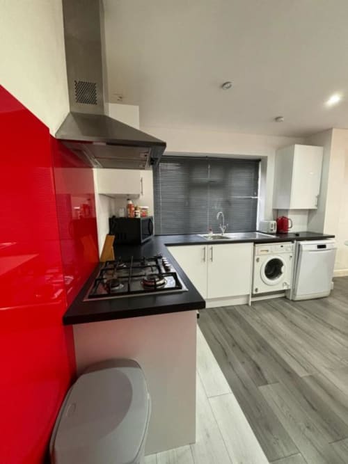 Modern kitchen at Sunbeam Haven bungalow with red splashback, black countertops, gas hob, and white appliances