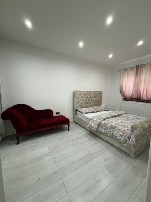 Modern bedroom with upholstered bed, burgundy chaise lounge, light wood flooring, and pink curtains at Sunbeam Haven villa