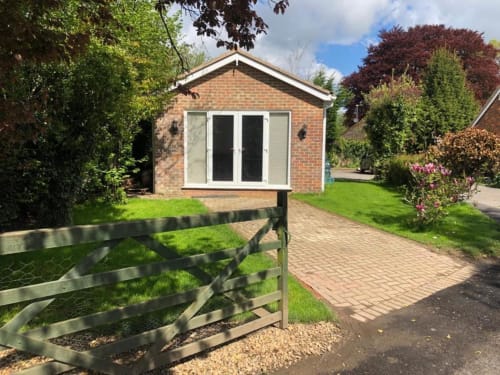 Modern brick bungalow with large windows, wooden gate, brick patio, and lush green garden at Sunbeam Haven in High Wycombe