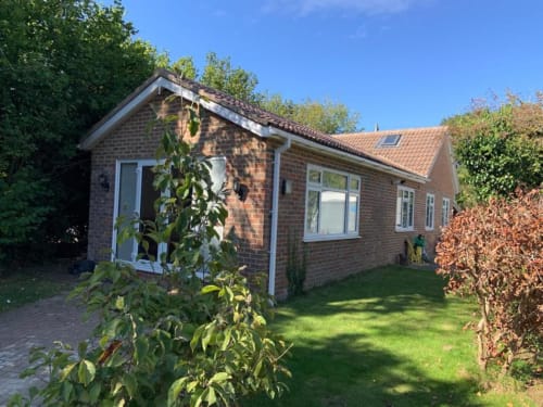 Sunbeam Haven 2BR brick bungalow in High Wycombe with green lawn, garden view, and white framed windows on a sunny day