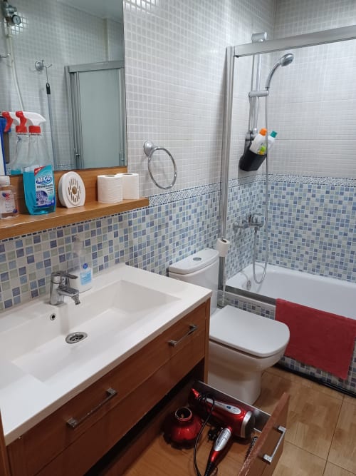 Baño moderno en Casa Ferrer Barcelona con azulejos blancos, mueble de madera, inodoro, ducha y toalla roja