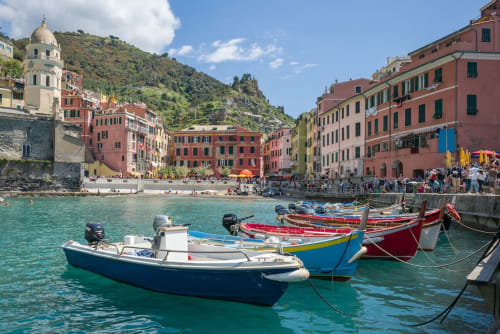 Barche da pesca colorate nelle acque turchesi di Vernazzo, villaggio italiano con edifici rossi e collina