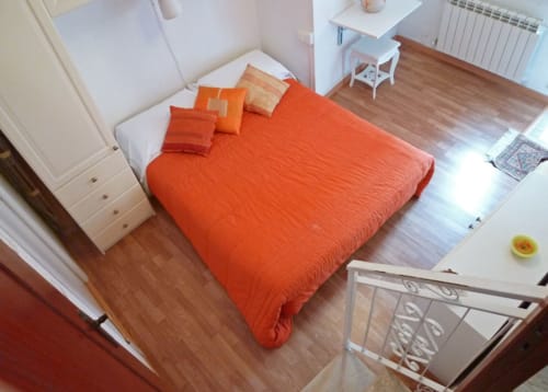 Camera luminosa della SoleMagia B&B a Vernazzo con letto arancio, testata bianca e pavimento in legno
