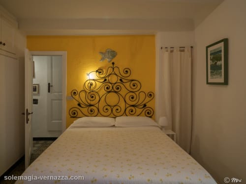 Camera da letto SoleMagia B&B a Vernazza con testata in ferro battuto ornamentale, parete accent dorata e servizi moderni