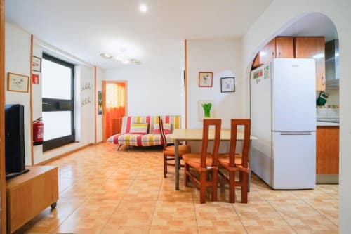 Área común de Casa Ferrer Barcelona con mesa de comedor, sofá colorido, refrigerador blanco y suelos de terracota