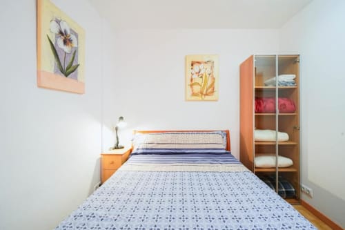 Dormitorio luminoso en Casa Ferrer Barcelona con cama de estampado azul, mesilla naranja y arte floral en la pared