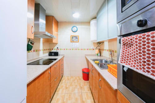 Bright galley kitchen at Casa Ferrer Barcelona with orange cabinets, stainless steel appliances, and colorful tile accents