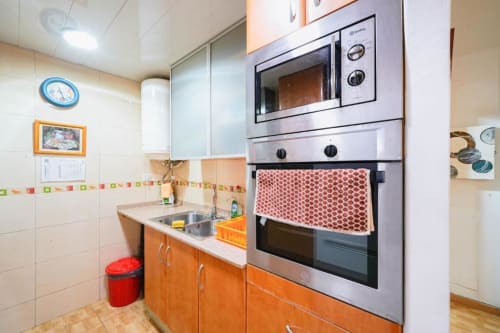 Cocina moderna con gabinetes naranjas, electrodomésticos de acero inoxidable y paredes de azulejos blancos en Casa Ferrer Barcelona