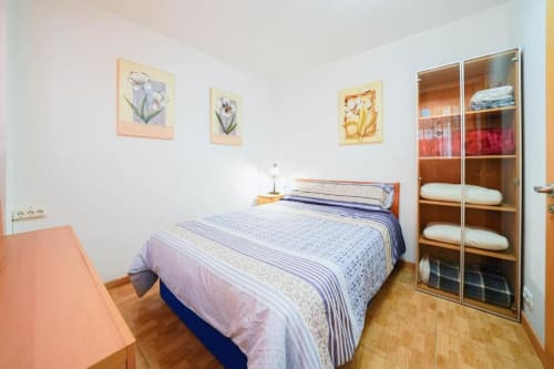 Acogedor dormitorio en Casa Ferrer Barcelona con ropa de cama azul rayada, suelos de madera, arte floral en la pared y armario de cristal