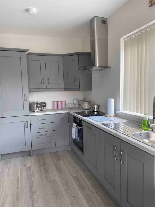 Modern gray kitchen at Duffy Lodge, Co. Donegal with stainless steel appliances, white countertops, and ample storage.