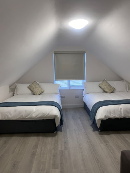Bright attic bedroom at Duffy Lodge with two twin beds, white linens, patterned pillows, wooden floors, and skylights in Co.