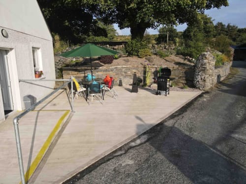 Outdoor patio at Duffy Lodge in Co Donegal with seating, green umbrella, BBQ grill, and tiered garden beyond.