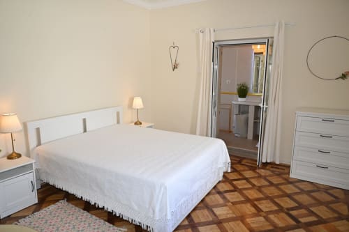 Chambre lumineuse à Villa Sor avec lit blanc, parquets en bois et salle de bain attenante à Ponte de Sor