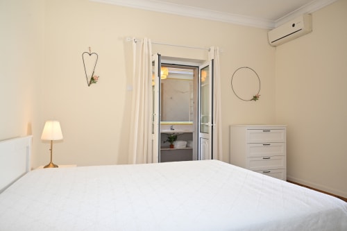 Chambre lumineuse à Villa Sor avec lit blanc, salle de bain attenante, commode en bois et décor épuré à Ponte de Sor