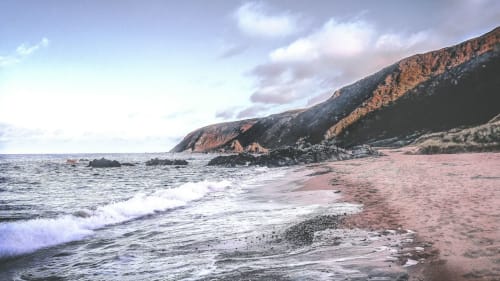 Rugged coastal beach at Duffy Lodge, County Donegal, with waves, red sand, and dramatic cliffside landscape