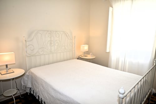 Quarto luminoso na Villa Sor em Ponte de Sor com cama de estrutura metálica branca, roupa de cama creme e luz natural das janelas