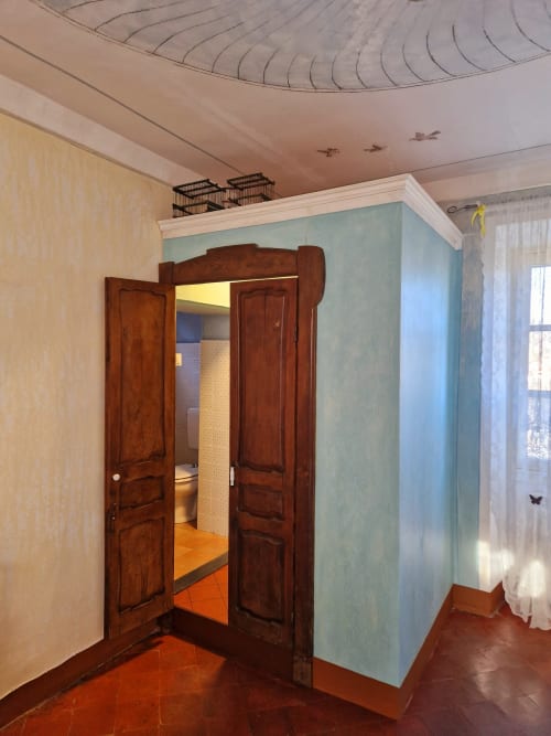 Doppie porte in legno che si aprono sulla camera da letto della B&B La Corte a Ovada, con parete celeste e finestra con vista sul giardino