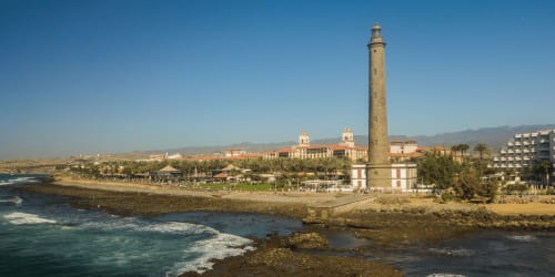Faro de Maspalomas y complejo de playa con palmeras y arquitectura costera en Las Palmas, España